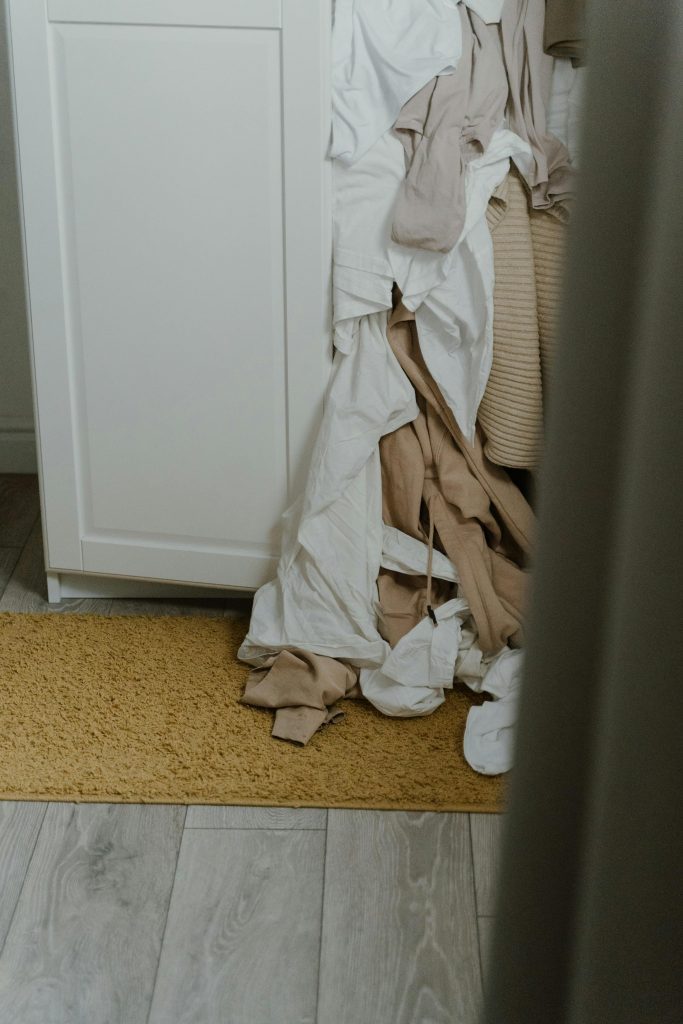 A white wardrobe overflowing with messy clothes spilling onto the floor clearly reflects the lack of storage space at home.